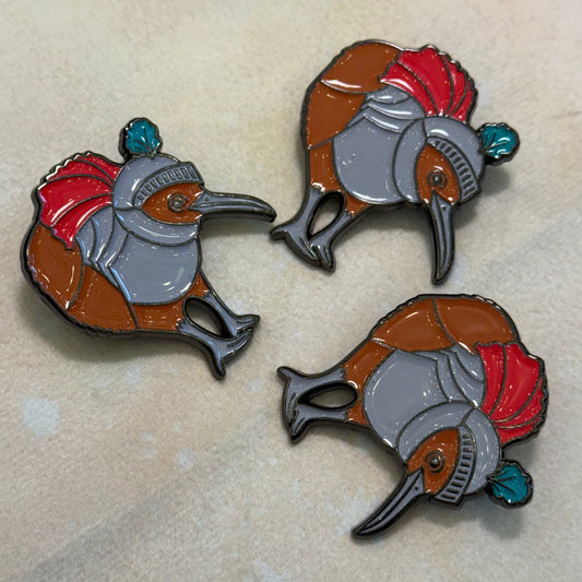 Three kiwi-shaped pins with suits of armor on a beige background